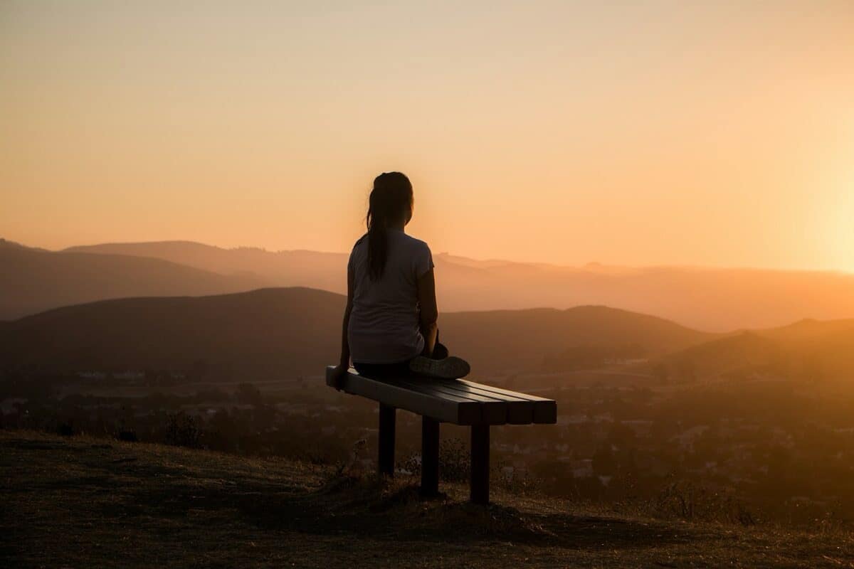 Femme assise face à un paysage paisible au coucher du soleil, sensation de calme retrouvé